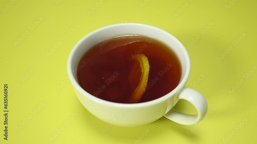 sugar is put in a cup with tea and lemon. White cup of tea on yellow background, top view, slow motion sugar is put in a cup with tea and lemon. White cup of tea on yellow background, top view, slow motion