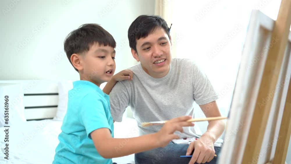 Happy Asian little boy enjoy drawing and painting a water color on a canvas with his father in the free time at home. Father teaching his son to draw and paint a picture. Creativity skill development. Happy Asian little boy enjoy drawing and painting a water color on a canvas with his father in the free time at home. Father teaching his son to draw and paint a picture. Creativity skill development.