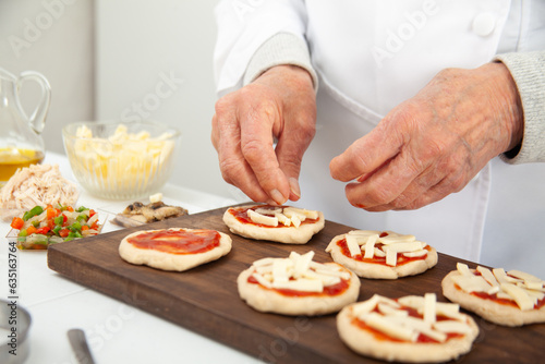 Adding toppings to the mini pizzas. Adding cheese. Delicious homemade mini pizzas preparation.