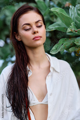Beauty portrait of a woman with wet hair in a white shirt near the leaves of a tropical tree, beauty and health tanned skin