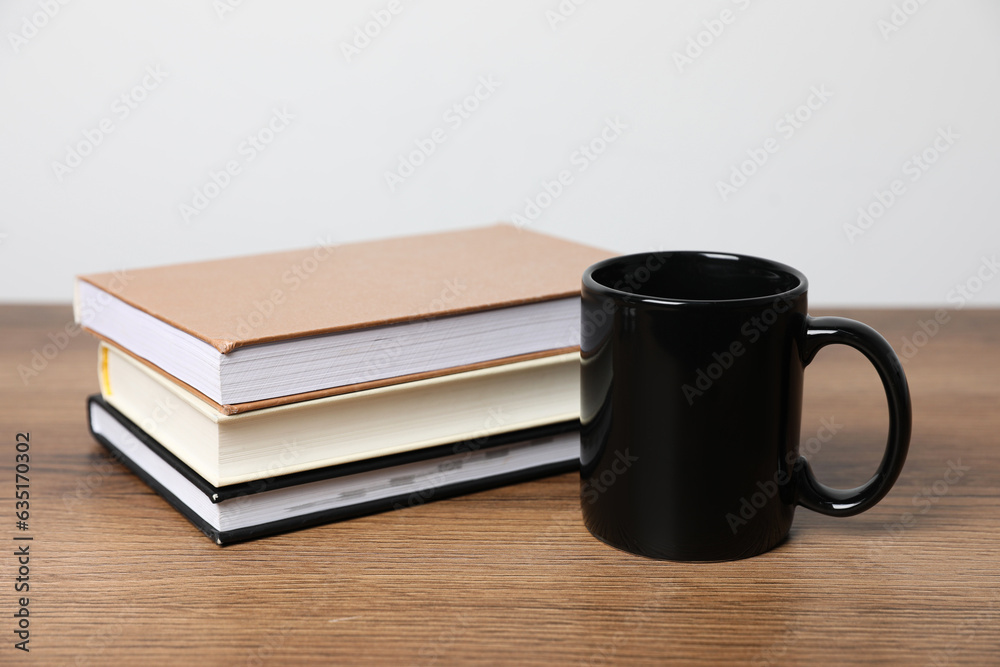 Black ceramic mug and stack of books on wooden table Black ceramic mug and stack of books on wooden table