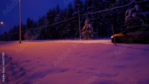 evening snowy road, car is passing by, shining headlights, thick layer of snow on trees, autotourism in Lapland, polar night, snowfall in forest, seasonal change of weather concept, beauty of Arctic photo