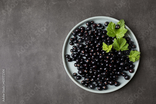Plate with ripe blackcurrants and leaves on grey background, top view. Space for text