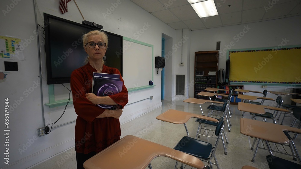 Portrait of sad unhappy teacher in an empty classroom with the lights turned off during budget cuts or a pandemic wondering about the future of education. Portrait of sad unhappy teacher in an empty classroom with the lights turned off during budget cuts or a pandemic wondering about the future of education.
