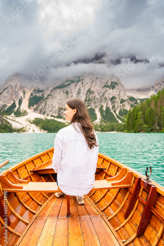 Woman sitting in big brown boat at Lago Braies lake in cloudy day, Italy. Summer vacation in Europe