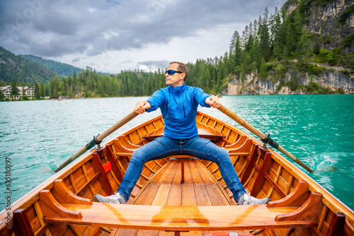 Man sitting in big brown boat at Lago di Braies lake in cloudy day  Italy. Summer vacation in Europe