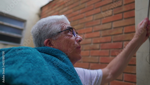 Elderly Man putting towels on shoulder after removing them from clothelines, doing domestic household chores activities photo