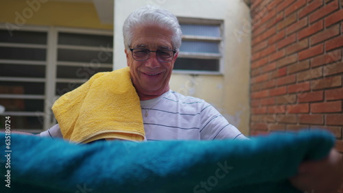 Elderly Man putting towels on shoulder after removing them from clothelines, doing domestic household chores activities photo