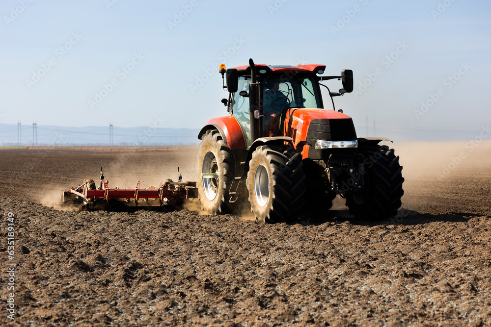 Fototapeta premium Tractor preparing land for sowing. Tractor with cultivator handles field before planting. Preparing land for sowing at spring, .