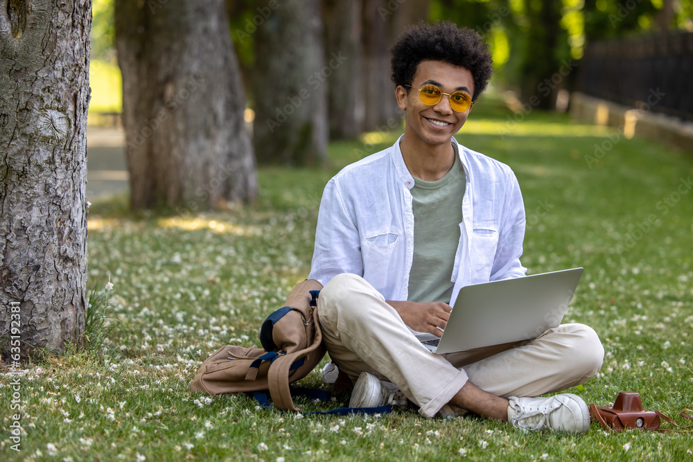 Man in light clothes sitting on the grass and working on laptop Man in light clothes sitting on the grass and working on laptop