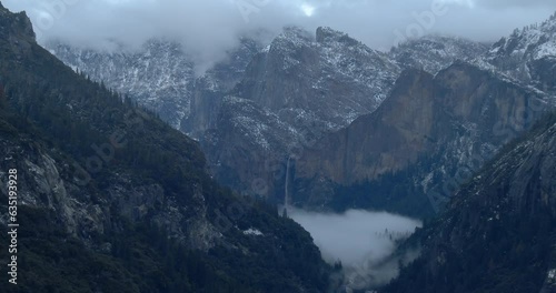 Storm clouds fill Yosemite Valley with Bridal Veil Falls flowing into canyon in winter