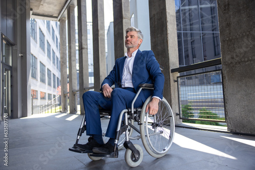 Gray haired disabled man wearing official style suit in wheelchair city background. © zinkevych