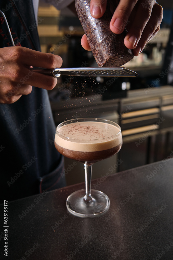 Barista decorating martini cocktail with grated chocolate in bar