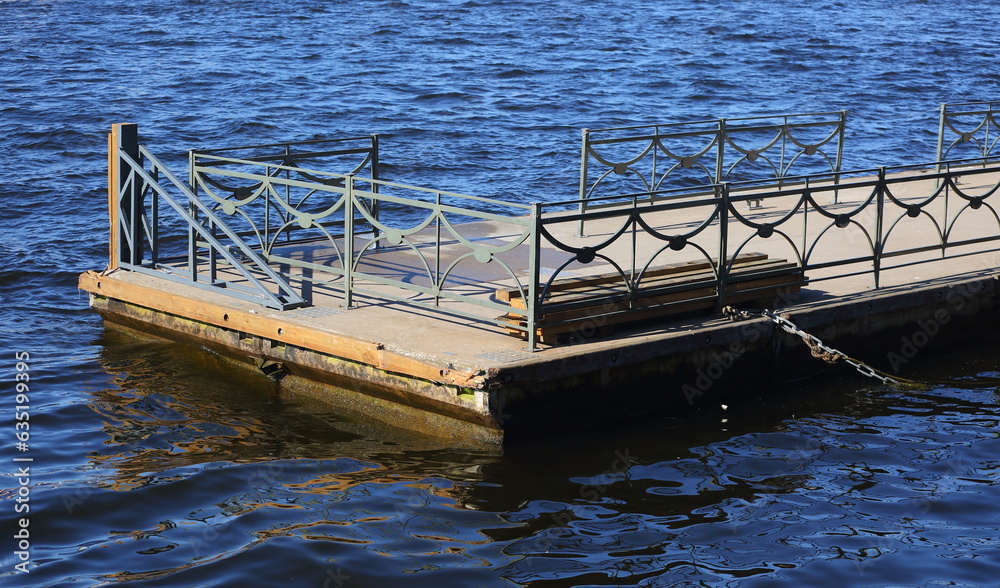 Floating wooden pier with metal fence in blue water Floating wooden pier with metal fence in blue water