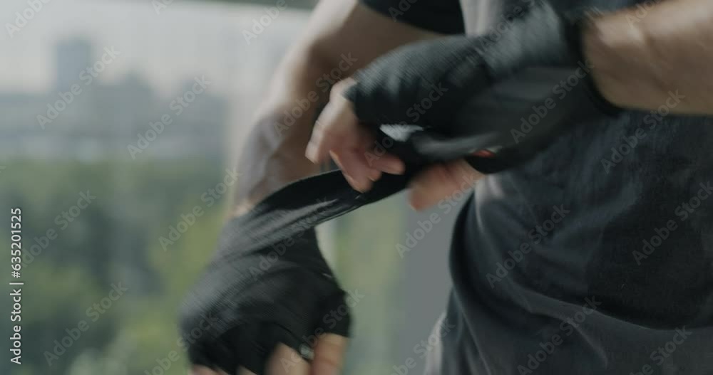 Close-up of male hands wrapping with straps preparing for boxing match while sportsman training in gym. Active lifestyle and martial arts concept. Close-up of male hands wrapping with straps preparing for boxing match while sportsman training in gym. Active lifestyle and martial arts concept.