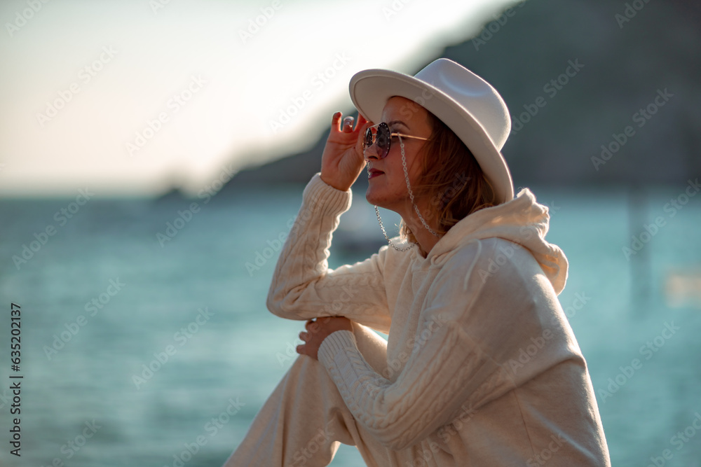 Happy blonde woman in a white suit and hat posing at the camera against the backdrop of the sea