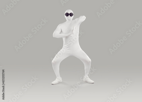 Funny man in bodysuit. Full length shot of happy young man disguised in white spandex fancy dress Halloween party body suit costume and black round sunglasses dancing on gray studio background photo