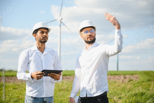 Two engineers discussing against turbines on wind turbine farm. photo