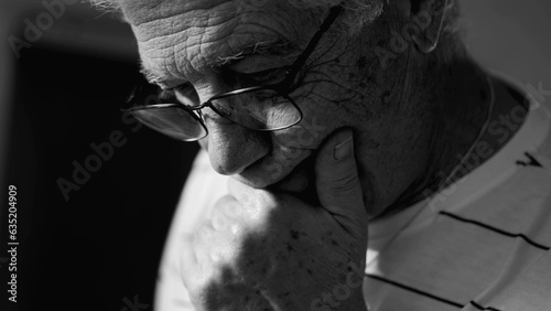 Senior man considering options in monochrome black and white. Dramatic elderly person ponders problems with hand in chin photo