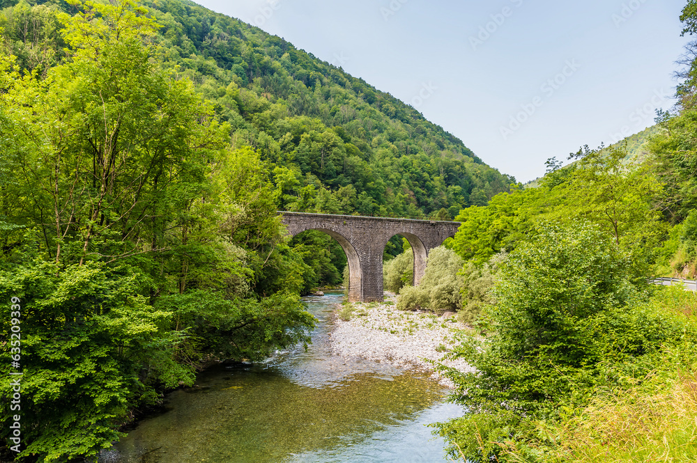 A view towards a stone arch railway bridge  over the River Baca near the village of Klavze in Slovenia in summertime
