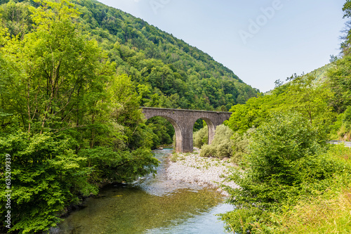 A view towards a stone arch railway bridge over the River Baca near the village of Klavze in Slovenia in summertime