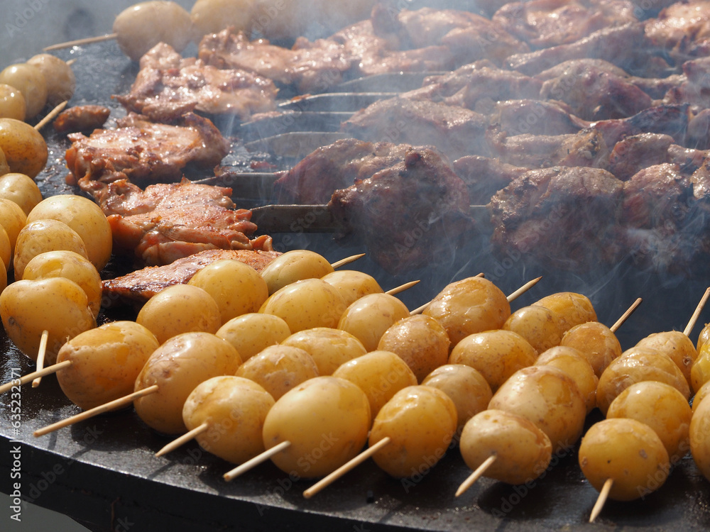 Potatoes, delicious fried tubers, with a golden crust, grilled, on the background of a brazier and fire. Fried potatoes, on skewers, close-up.