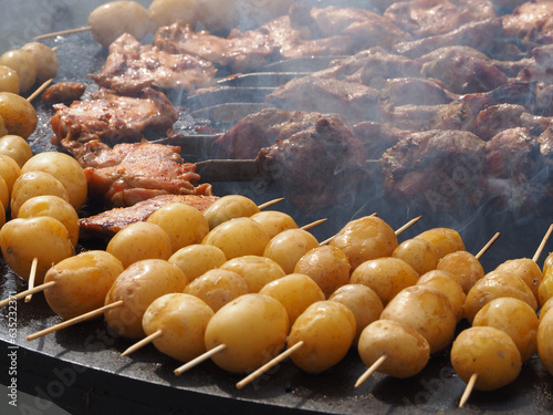 Obraz na płótnie Potatoes, delicious fried tubers, with a golden crust, grilled, on the background of a brazier and fire. Fried potatoes, on skewers, close-up. w salonie