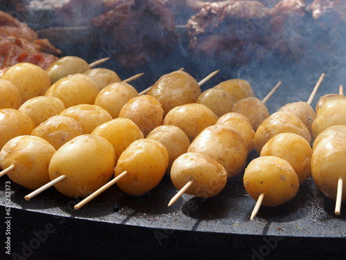 Obraz na płótnie Potatoes, delicious fried tubers, with a golden crust, grilled, on the background of a brazier and fire. Fried potatoes, on skewers, close-up. w salonie