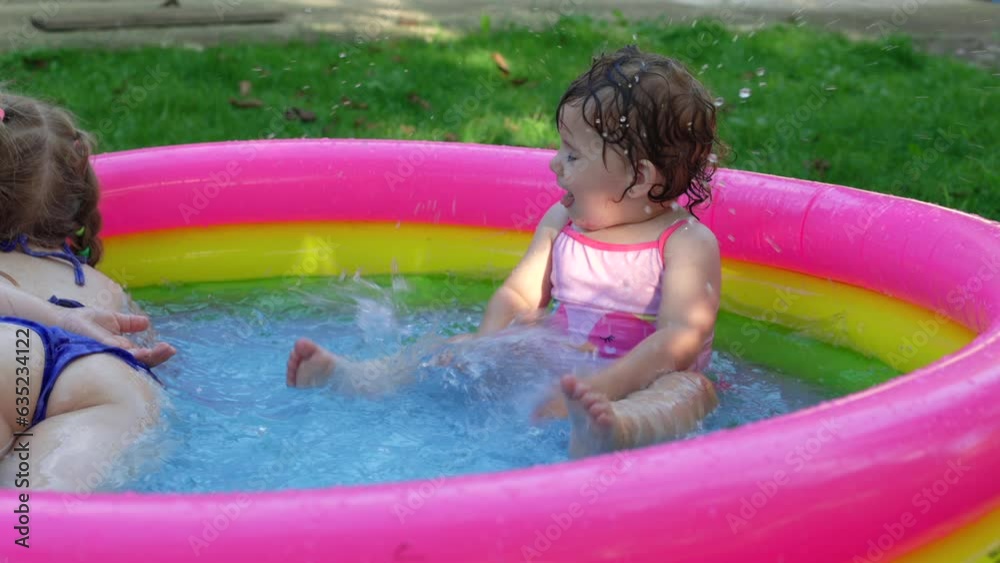 Children in the pool, it's hot in the summer. A little girl. A child plays in a children's pool. Swimming in the yard, inflatable pool in the shade. The girl loves water. Happy child in a swimsuit
