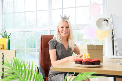 Mature woman with birthday gift and muffins in office