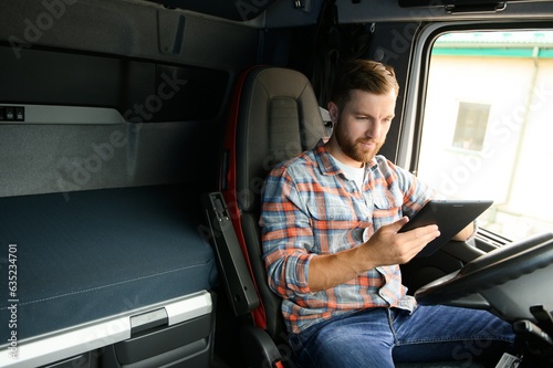 Man truck driver sitting behind wheel of car and holding digital tablet in his hands