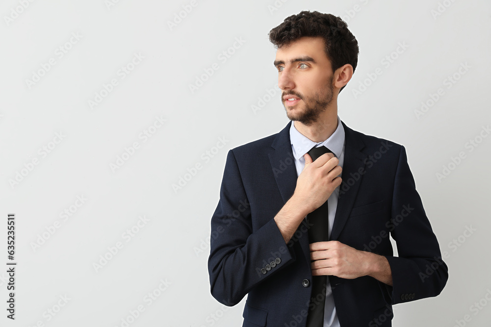 Young businessman in suit fixing necktie on light background Young businessman in suit fixing necktie on light background