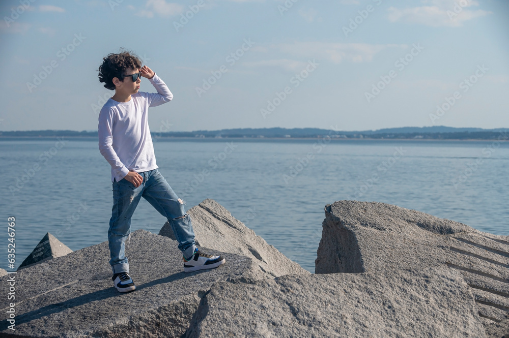 Boy in jeans and white pants with sunglasses posing for a photo in fashion editorial on the beach