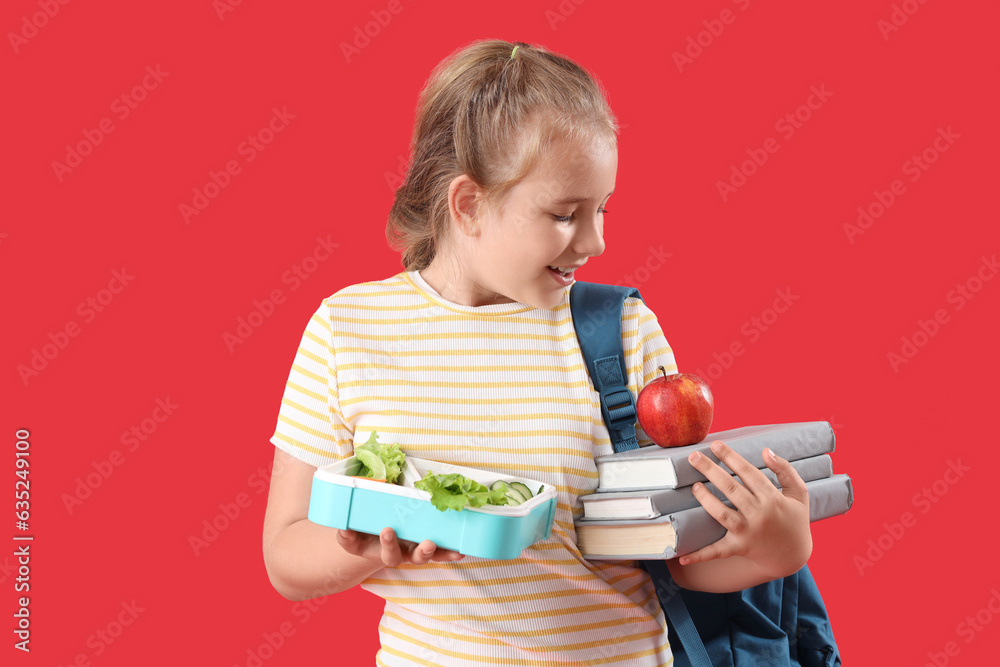 Happy little girl with lunchbox, apple and books on red background Happy little girl with lunchbox, apple and books on red background