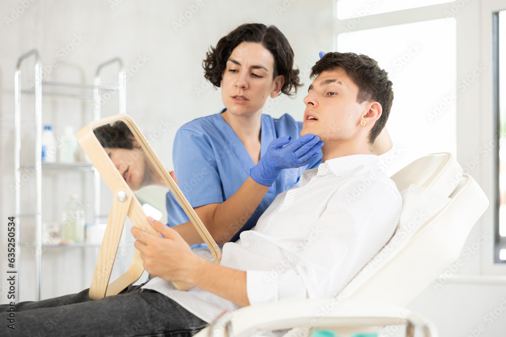 Obraz premium Middle-aged female doctor consulting young man patient lying on medical chair