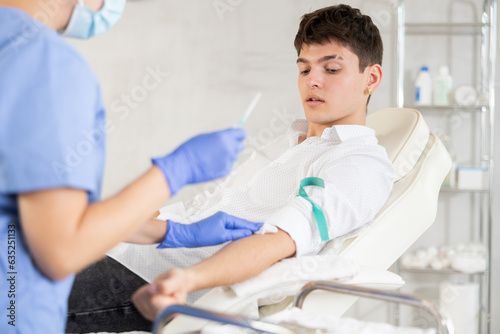 Young male patient lying on clinical chair having vein injection by young doctor