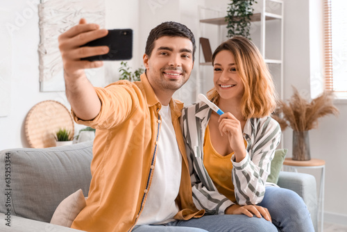Happy young couple with pregnancy test taking selfie at home