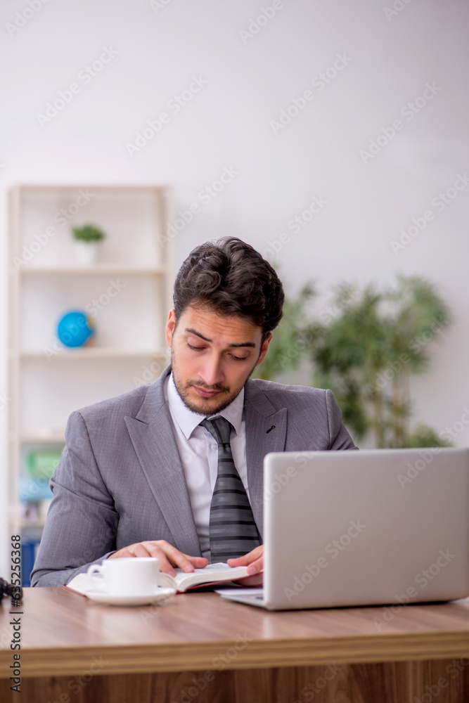 Young male employee reading book in the office