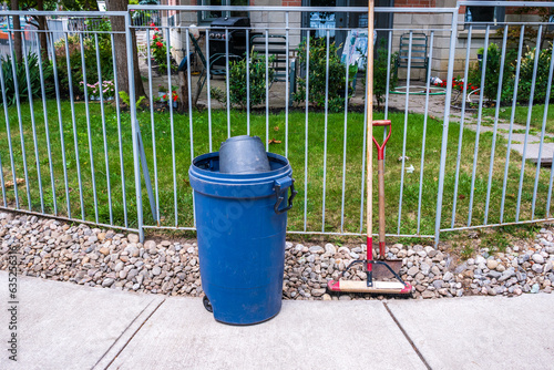 Wall Mural sidewalk clean up: refuse bins and tools lean against a fence above a pebble boa
