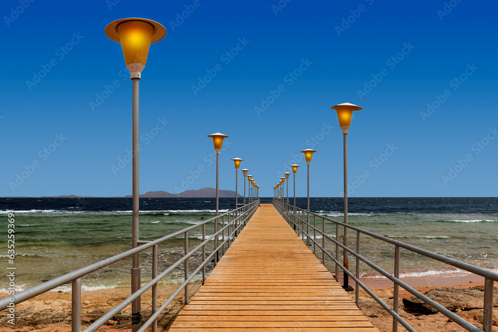 Wooden pier with streetlights on sea cost at dusk.