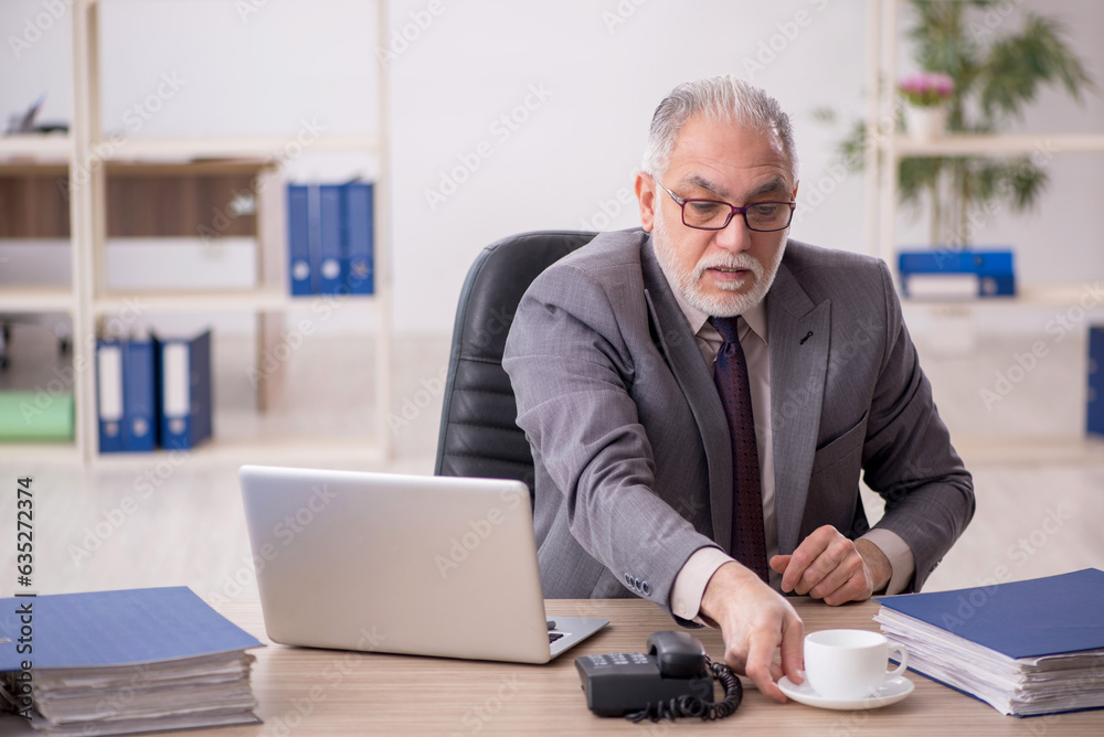 Old male employee drinking coffee in the office