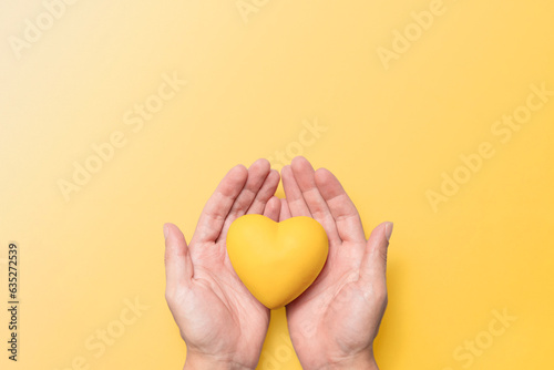 hands holding a yellow resin heart against a matching yellow background, symbolizing mental health awareness and the significance of September Yellow. Mental wellbeing and suicide prevention.