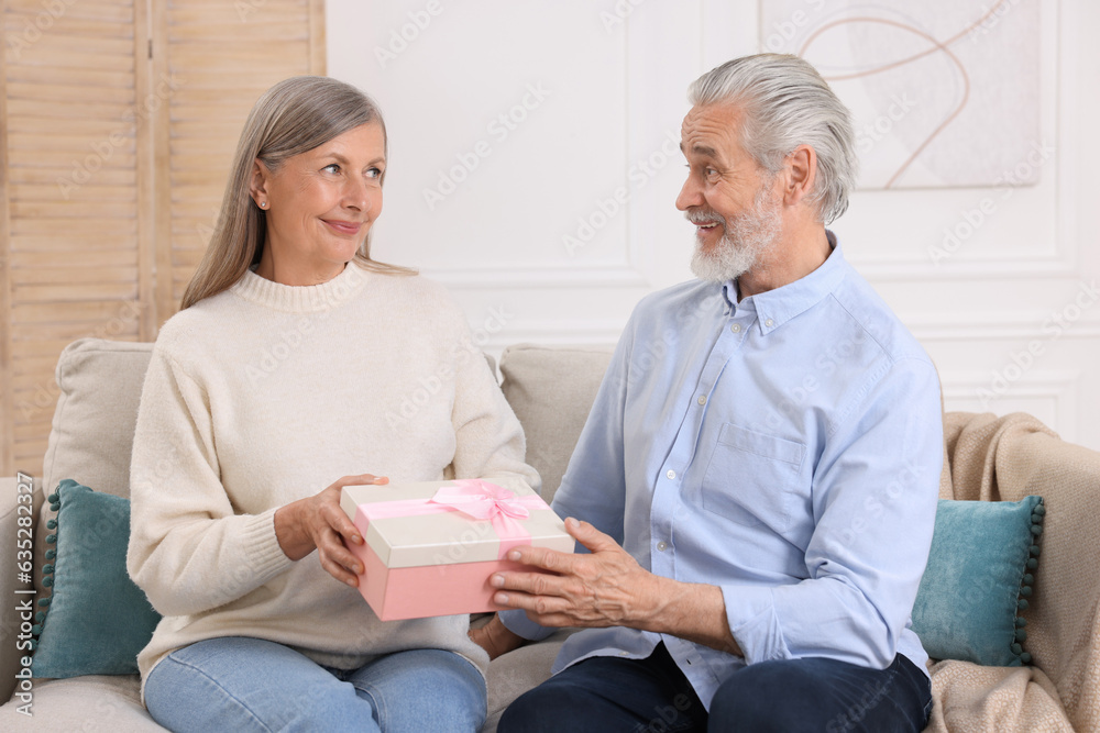 Happy affectionate senior couple with gift box on sofa indoors Happy affectionate senior couple with gift box on sofa indoors