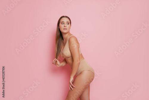 Closeup shot of sporty girl with long hair in beige sport underwear posing on pink background, natural beauty concept, copy space
