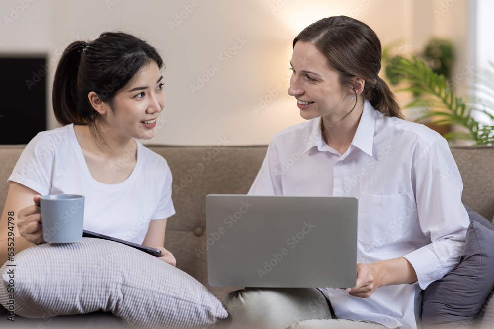 Two Happy asian Ladies Using Laptop Computer Working And Learning Online Together Or Making Video Call Sitting At on sofa in home . E-Learning. Females Entrepreneurship Career Concept.