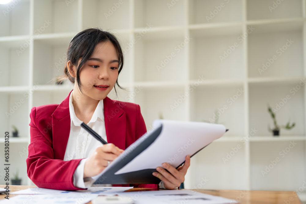 A beautiful Asian businesswoman focuses on examining a business report at her desk.
