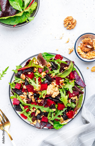 Healthy vegan salad with beet, dry prunes, arugula, swiss chard and walnuts, white table background. Fresh useful vegetarian dish for clean eating