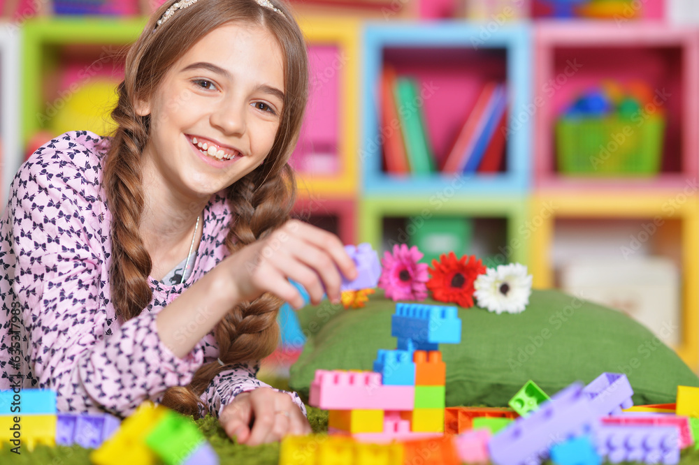 Fototapeta premium Portrait of cute girl playing with colorful plastic blocks in room
