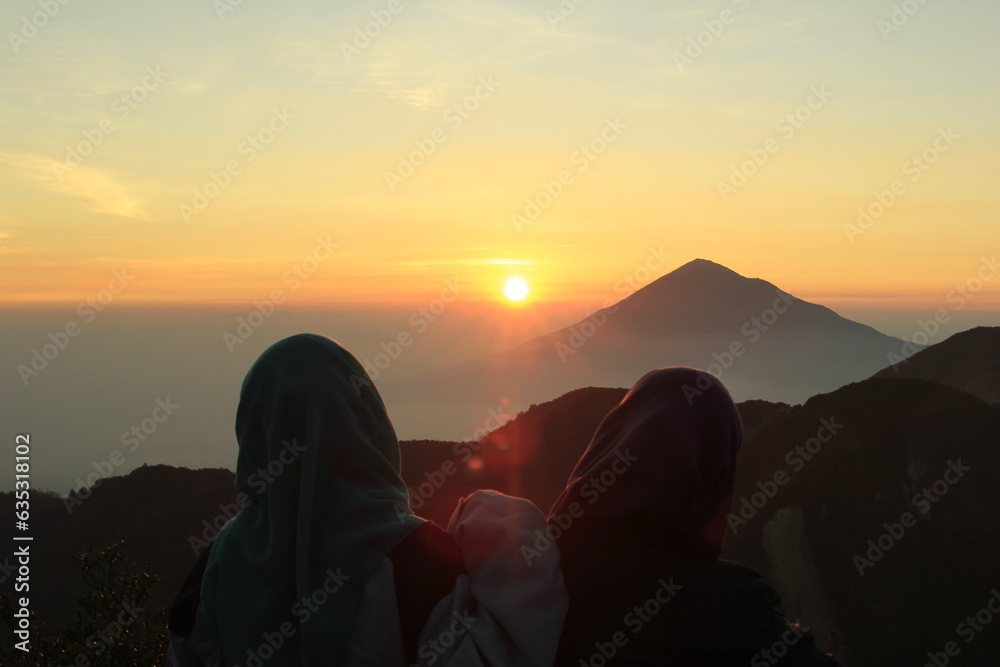 photo illustration of a pair of friends who are enjoying the beautiful sunrise from the top of mount papandayan