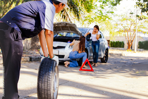 Emergency outdoor service technician changing tires while traveling : The difficult task of two beautiful women standing together to change a tire on a difficult road is getting help from a mechanic.